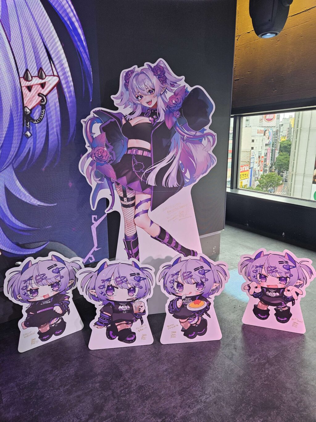 VTuberイバラ・デビルローズの等身大パネルと4体のデフォルメパネルが並ぶ展示スペース。背景の窓越し外の様子が見えている